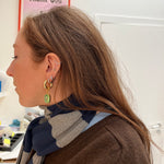 Woman wearing gold earrings with green gemstones in an office setting.