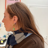 Woman wearing gold earrings with green gemstones in an office setting.
